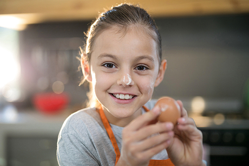 Close-up of smiling girl holding eggs with flour on her nose in the kitchen