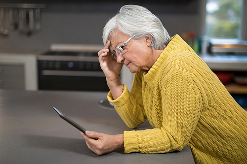 Tensed senior woman using digital tablet in the kitchen