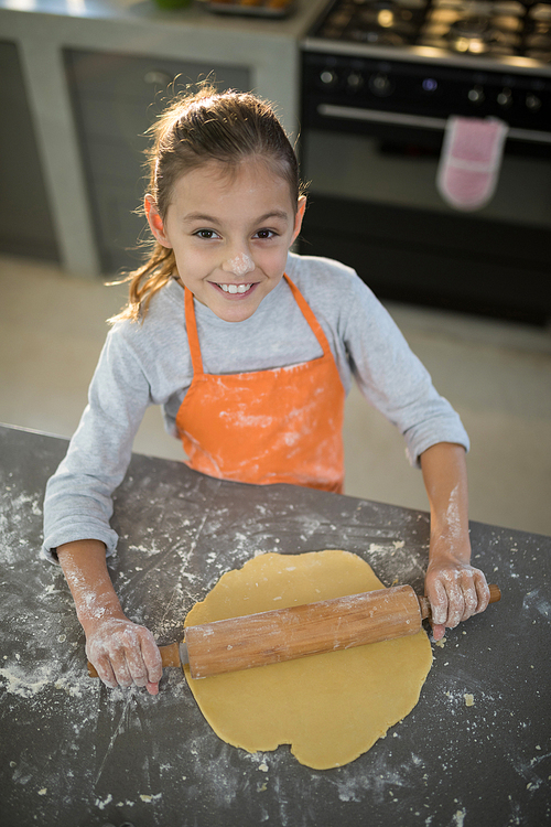 Portrait of little girl flattening dough on the kitchen counter