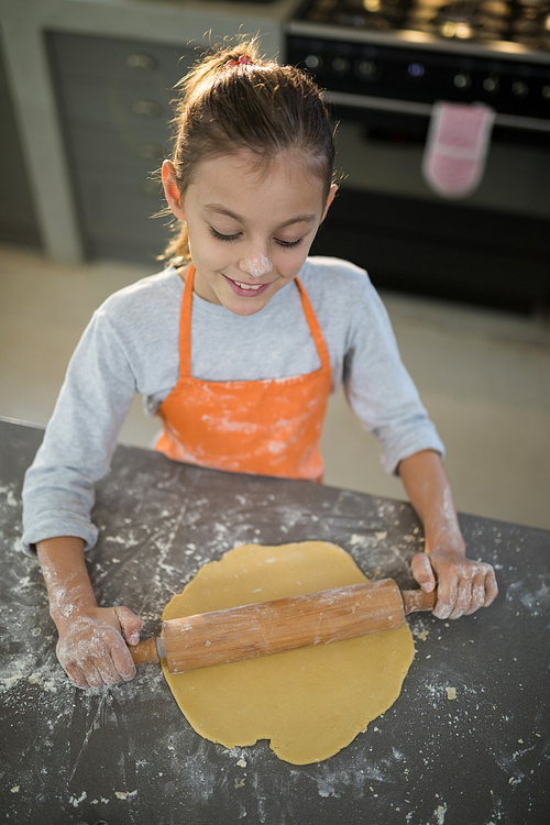 Close-up of little girl flattening dough on the kitchen counter