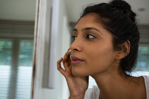 Woman touching face by mirror in bathroom at home