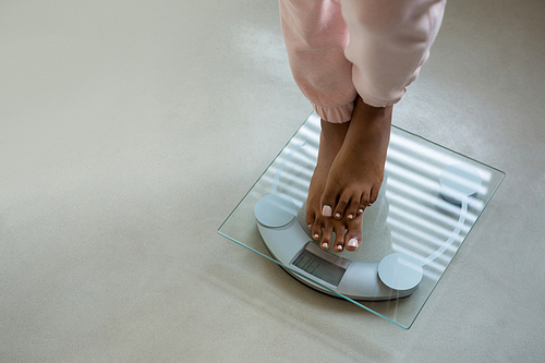 Low section of woman standing on bathroom scale at home