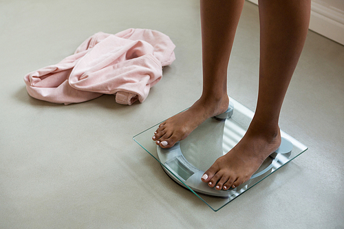 Low section of woman standing on bathroom scale at home
