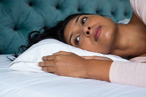 Thoughtful woman lying down on bed at home