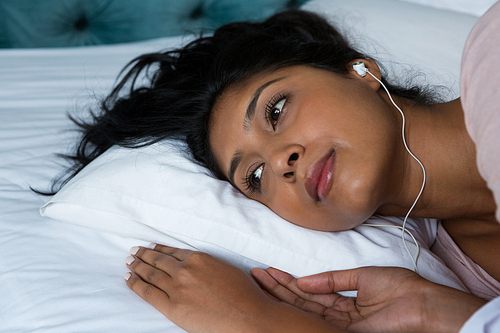 Thoughtful young woman listening to music on bed at home