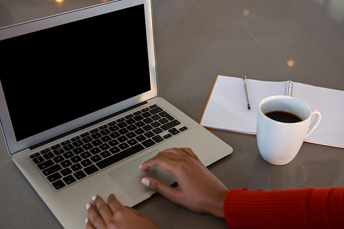 Cropped hands of woman using laptop by coffee cup at kitchen counter