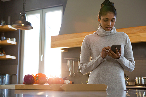 Young woman using phone in kitchen at home