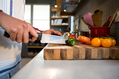 Mid section of woman cutting zucchini in kitchen at home