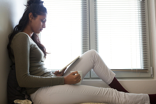 Side view of young woman with digital tablet by window at home