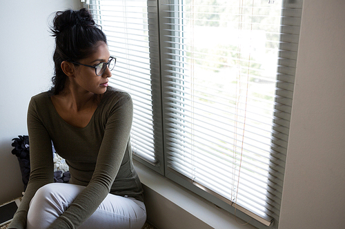 Thoughtful young woman by window at home