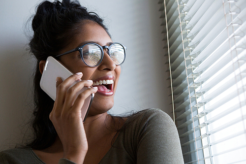 Happy young woman talking on phone by window at home