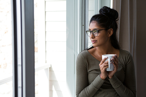 Young woman with coffee cup by window at home