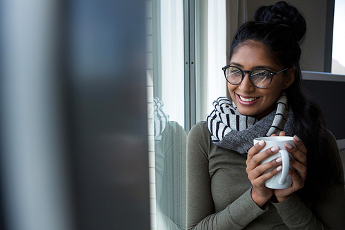 Smiling young woman with coffee cup by window at home