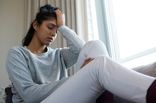 Tired young woman sitting on sofa at home