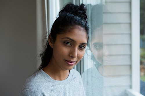 Portrait of young woman by glass window at home
