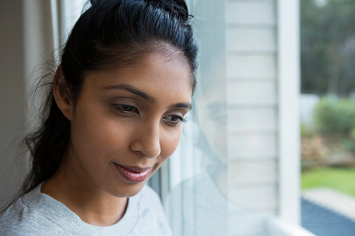 Thoughtful young woman by glass window at home