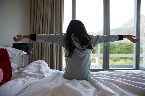 Rear view of girl with arms outstretched relaxing on bed at home