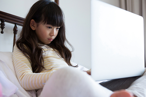 Girl with long hair using laptop while sitting on bed at home