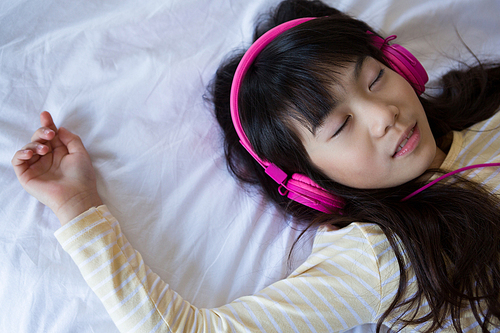 Girl with long hair listening to music while relaxing on bed at home