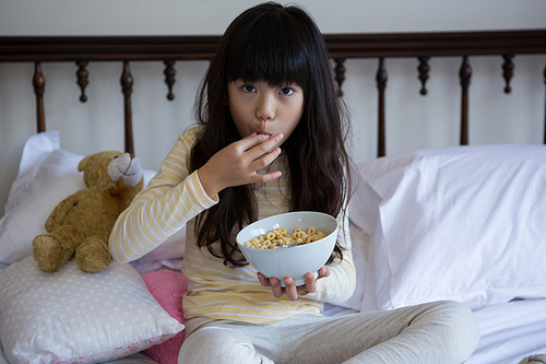 Portrait of girl eating breakfast on bed at home