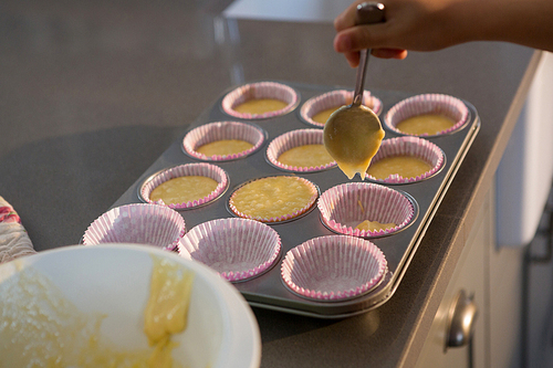 Cropped hand pouring batter in cupcake holder at kitchen counter
