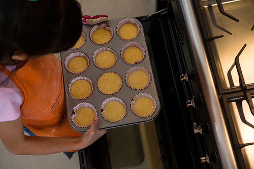 High angle view of girl keeping muffin tin in oven at home