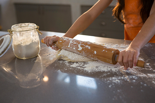 Cropped hands of girl rolling dough at kitchen counter