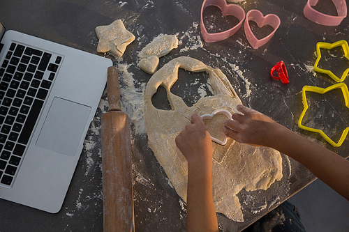 Cropped hands of girl making shape on dough by laptop in kitchen at home