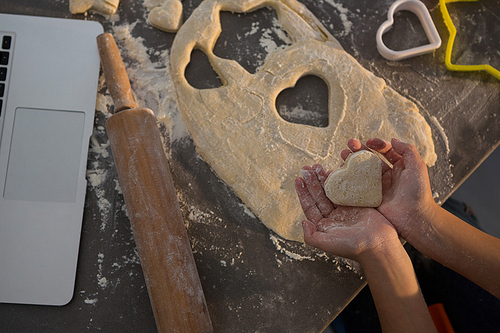Cropped hands of girl holding heart shape dough at kitchen counter