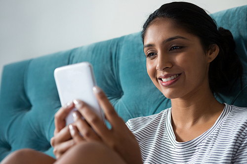 Smiling young woman using phone in bedroom at home