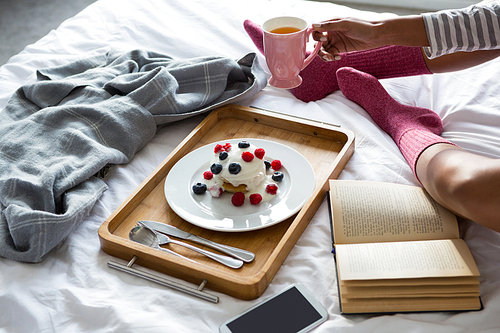 Low section of woman wih book doing breakfast on bed at home