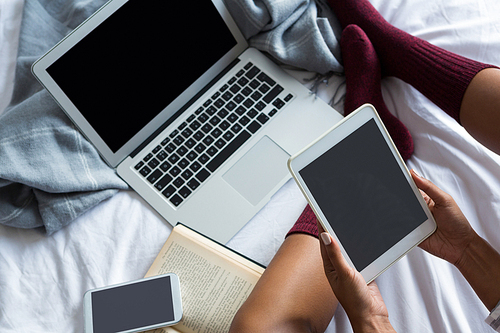 Low section of woman using digital tablet by laptop on bed at home