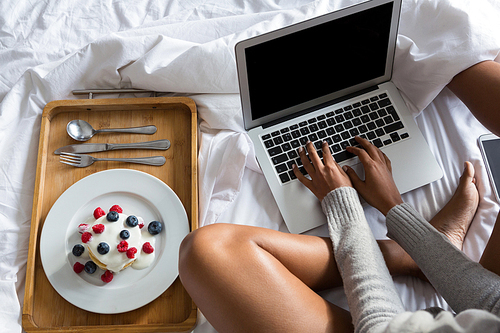 Low section of woman using laptop while relaxing by breakfast on bed at home