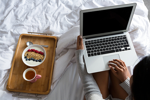 Woman using laptop by breakfast tray on bed at home