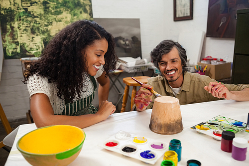 Man assisting woman in painting vase during drawing class