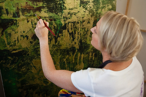 Attentive woman painting on canvas in drawing class