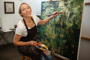 Portrait of happy woman painting on canvas in drawing class