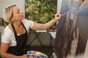 Attentive woman painting on canvas in drawing class