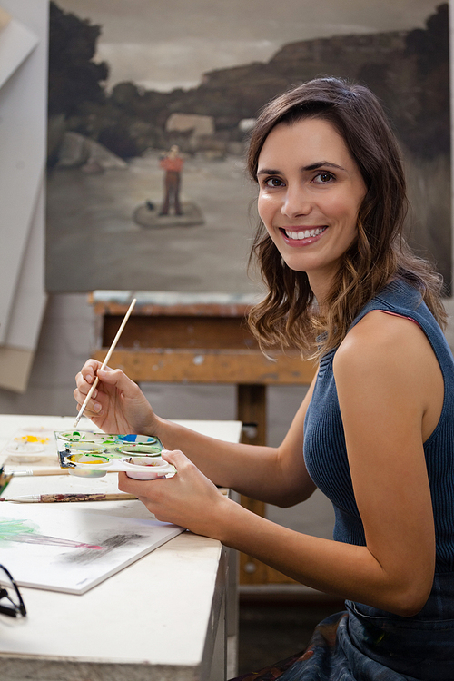 Portrait of smiling woman painting on drawing book in drawing class