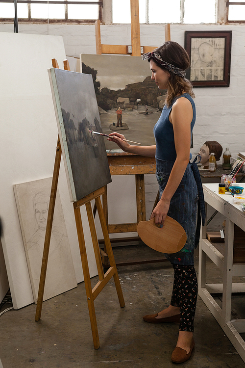 Attentive woman painting on canvas in drawing class