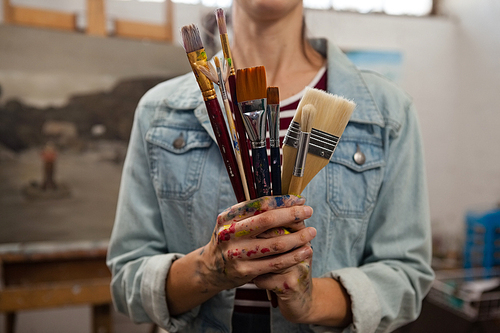 Mid-section of woman holding various brushes in drawing class