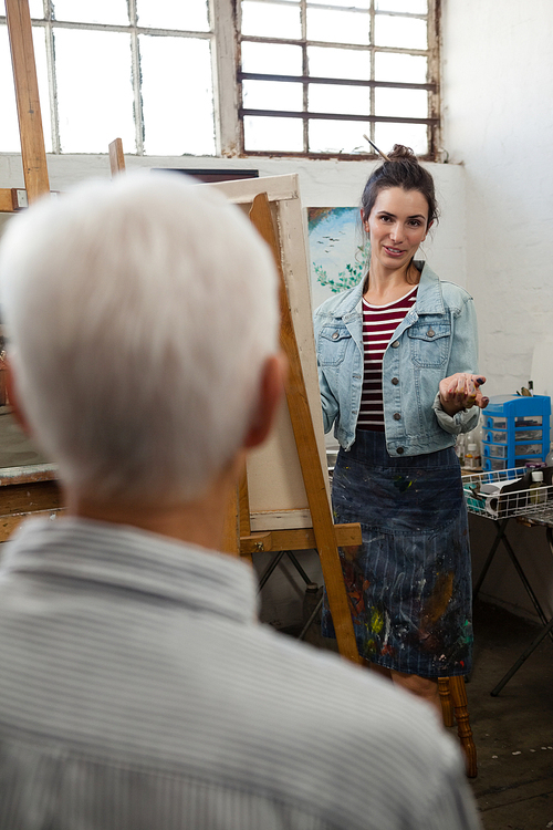 Woman interacting with senior man while painting on canvas in drawing class