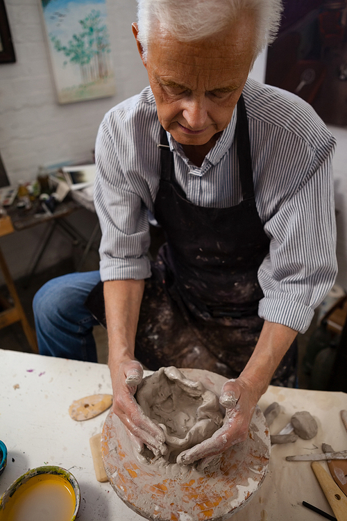 Attentive senior man molding clay in drawing class