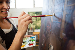 Attentive woman painting on canvas in drawing class