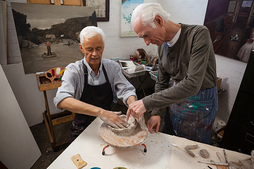 Attentive senior man assisting in making pottery during drawing class