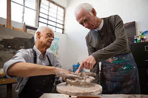 Attentive senior man assisting in making pottery during drawing class