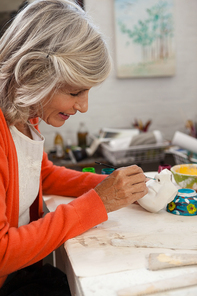 Attentive senior woman painting bowl in drawing class