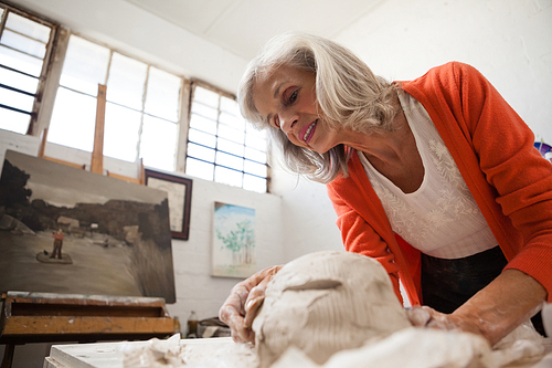 Attentive senior woman shaping a molded clay in drawing class