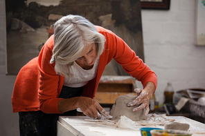 Attentive senior woman shaping a molded clay in drawing class