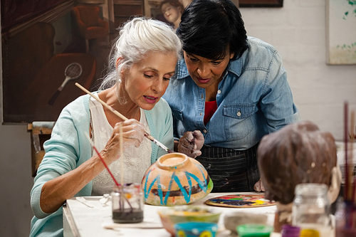 Attentive woman assisting senior woman in painting bowl at drawing class